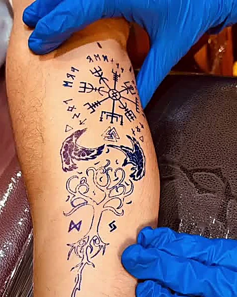 Diseño de vegvisir con árbol en estarcido azul sobre una pierna, sostenida con guantes azules, antes de tatuar