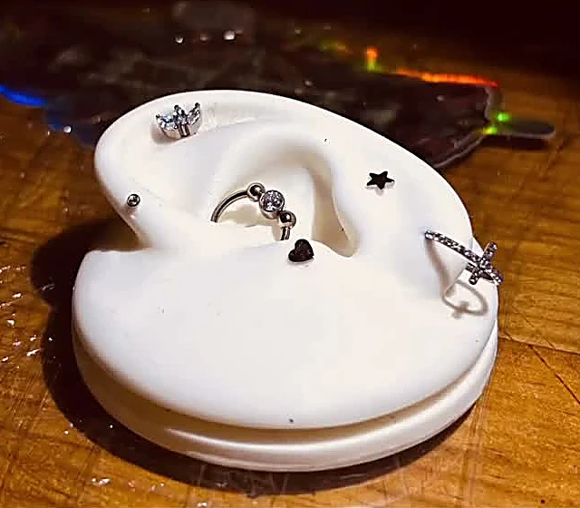 Oreja de silicón blanca con joyería puesta sobre la mesa de madera del estudio